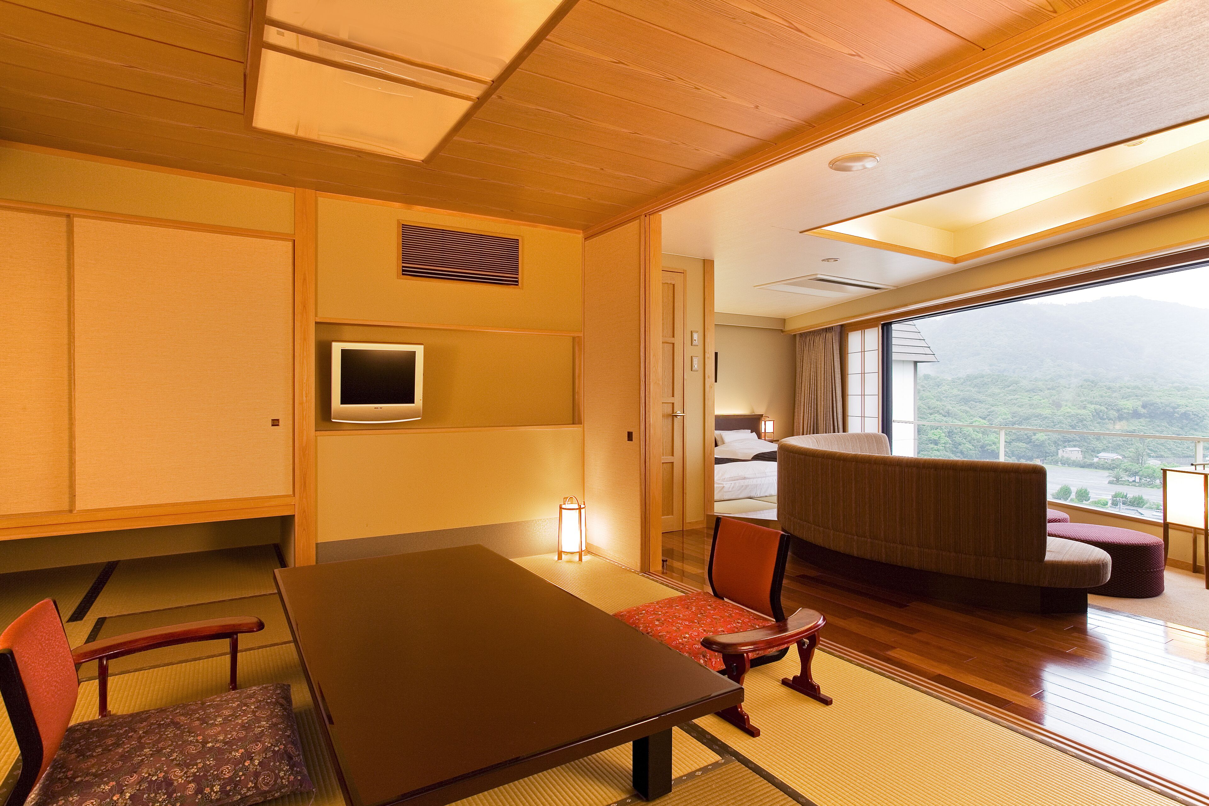 Hotelkamer met houten plafond, tatami vloer, een bed met uitzicht, een tafel, stoelen en een televisie.