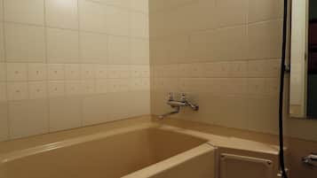 A bathroom with a bathtub, white tiled walls, and a shower area.
