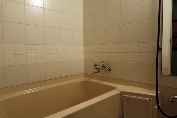 Un baño con bañera, paredes de azulejos blancos y zona de ducha.