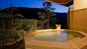Een whirlpool met een stenen rand, een houten pergola en een uitzicht op een bergachtig landschap in de schemering.