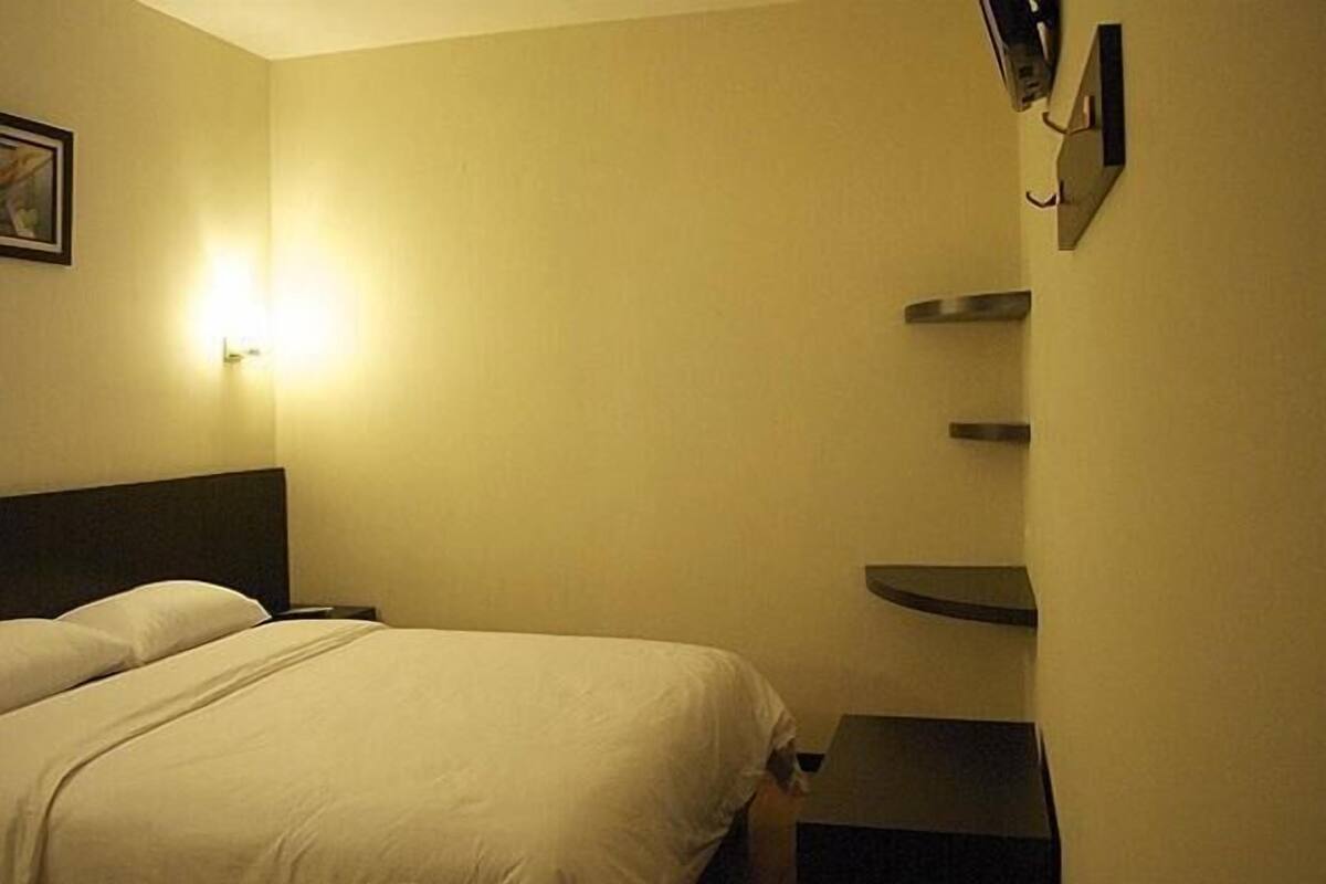 Hotellihuone, jossa on sänky, yöpöydät ja seinälle kiinnitetty hylly.