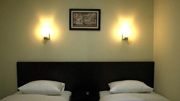 Habitación de hotel con dos camas individuales, un cabecero oscuro y dos lámparas fijadas a la pared.