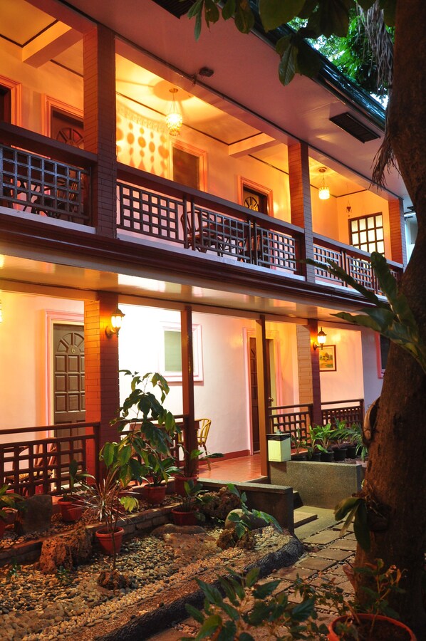 A two-story building with a balcony, potted plants, and a stone pathway.