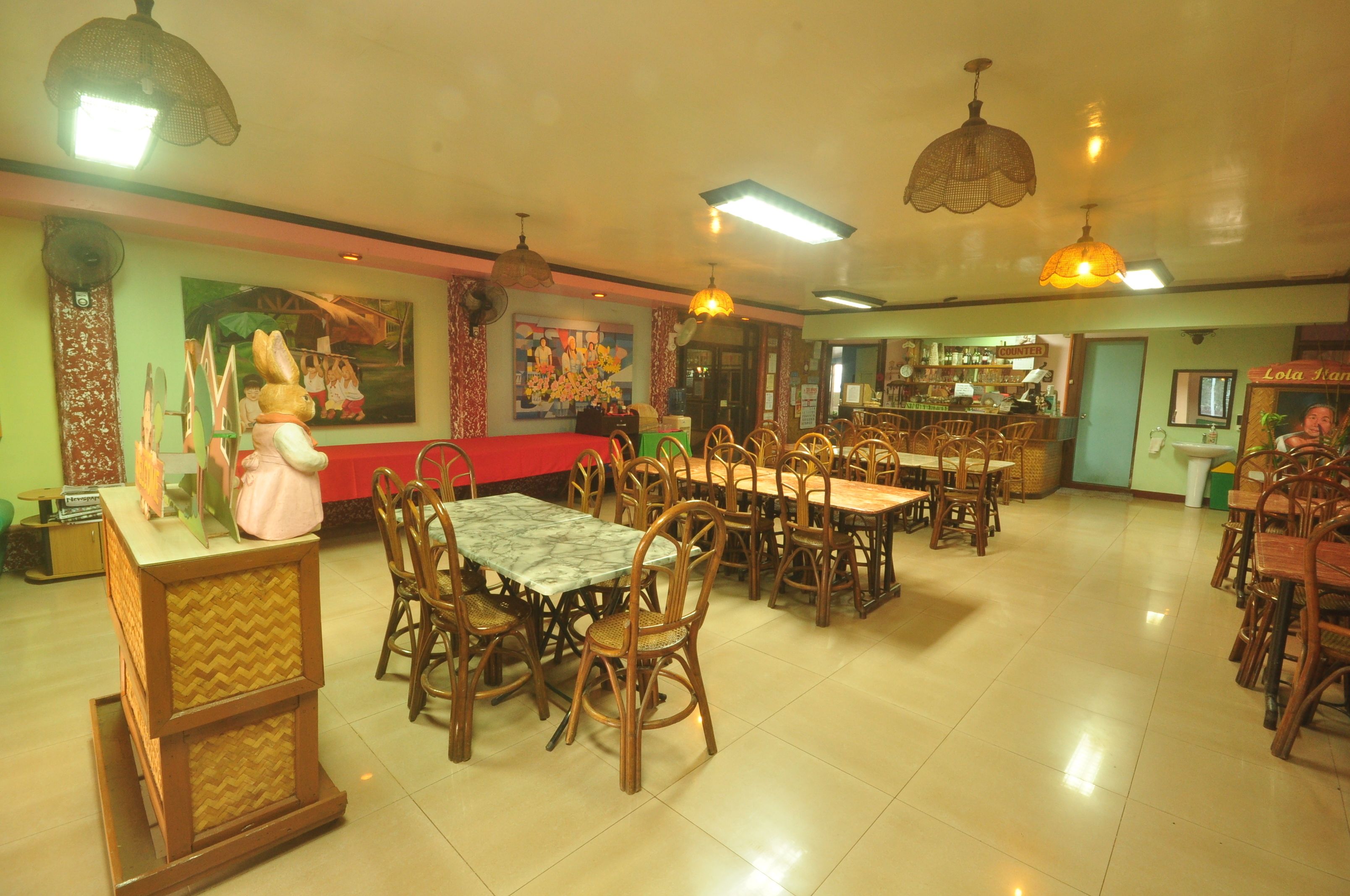 A restaurant with wooden tables and chairs, a counter with a cash register, and hanging pendant lights.
