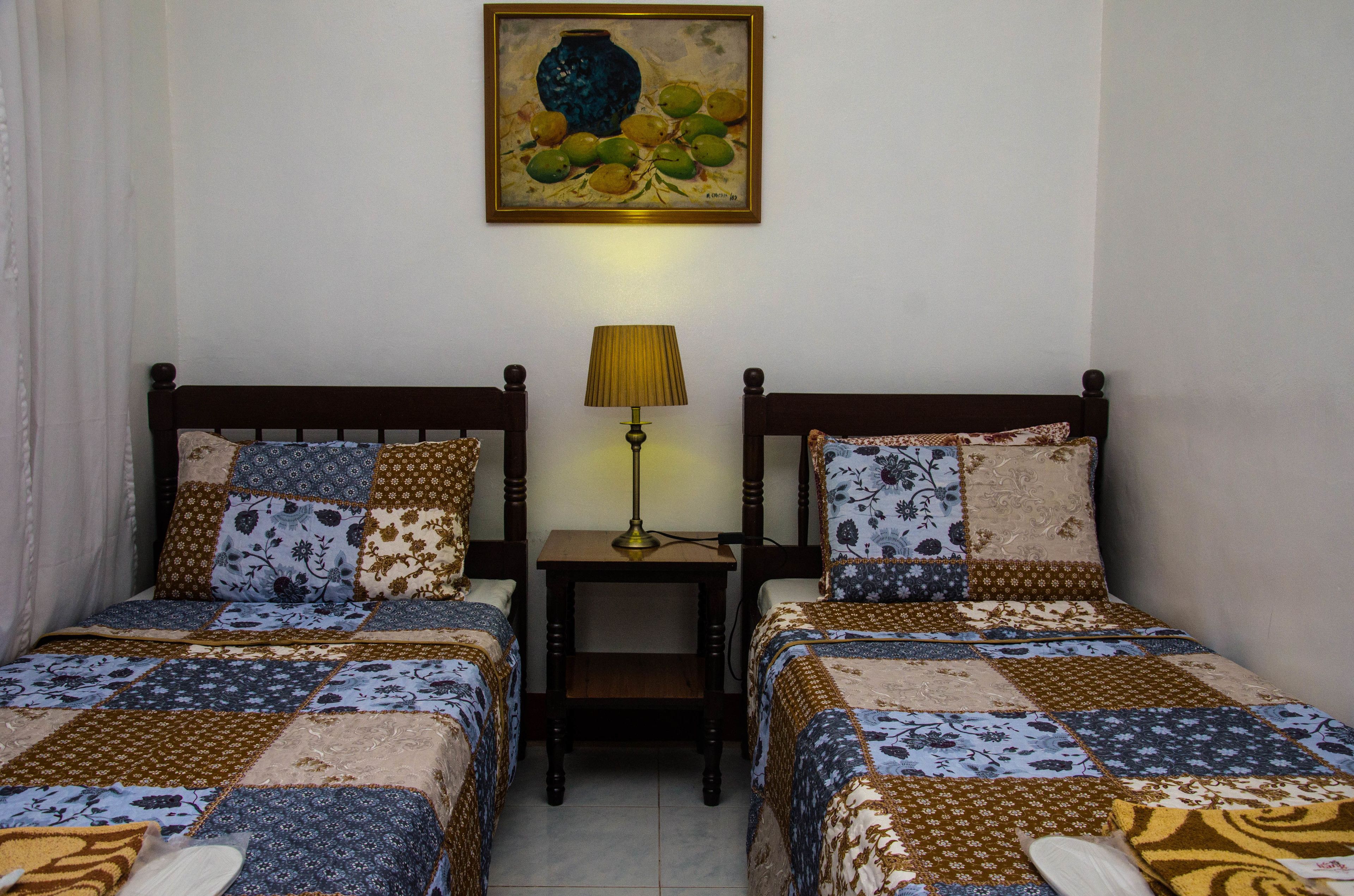 A bedroom with two beds, a nightstand with a lamp, and a painting on the wall.