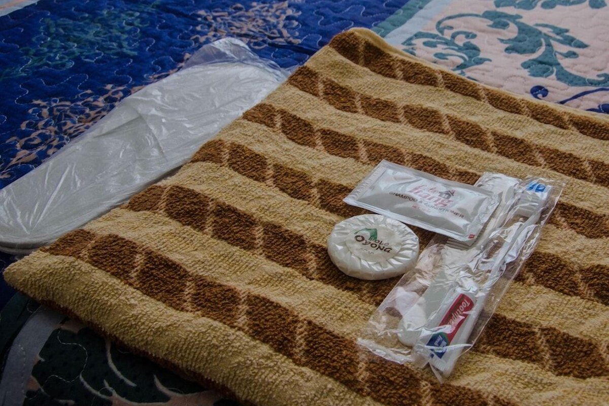 A bed with a brown and beige striped blanket, a white pillow, and a plastic bag containing toiletries.