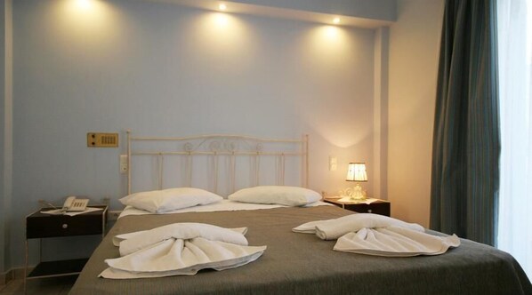 A neatly made bed with pillows and towels, a bedside phone, and a lamp on a nightstand.