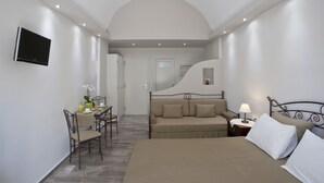 A bedroom with a bed, a sofa, a desk with a chair, a TV, and a lamp. - Preka Maria Hotel (Santorini)