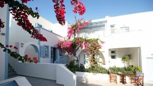A white building with blue shutters, a staircase, and a patio area with a table and chairs. - Preka Maria Hotel (Santorini)
