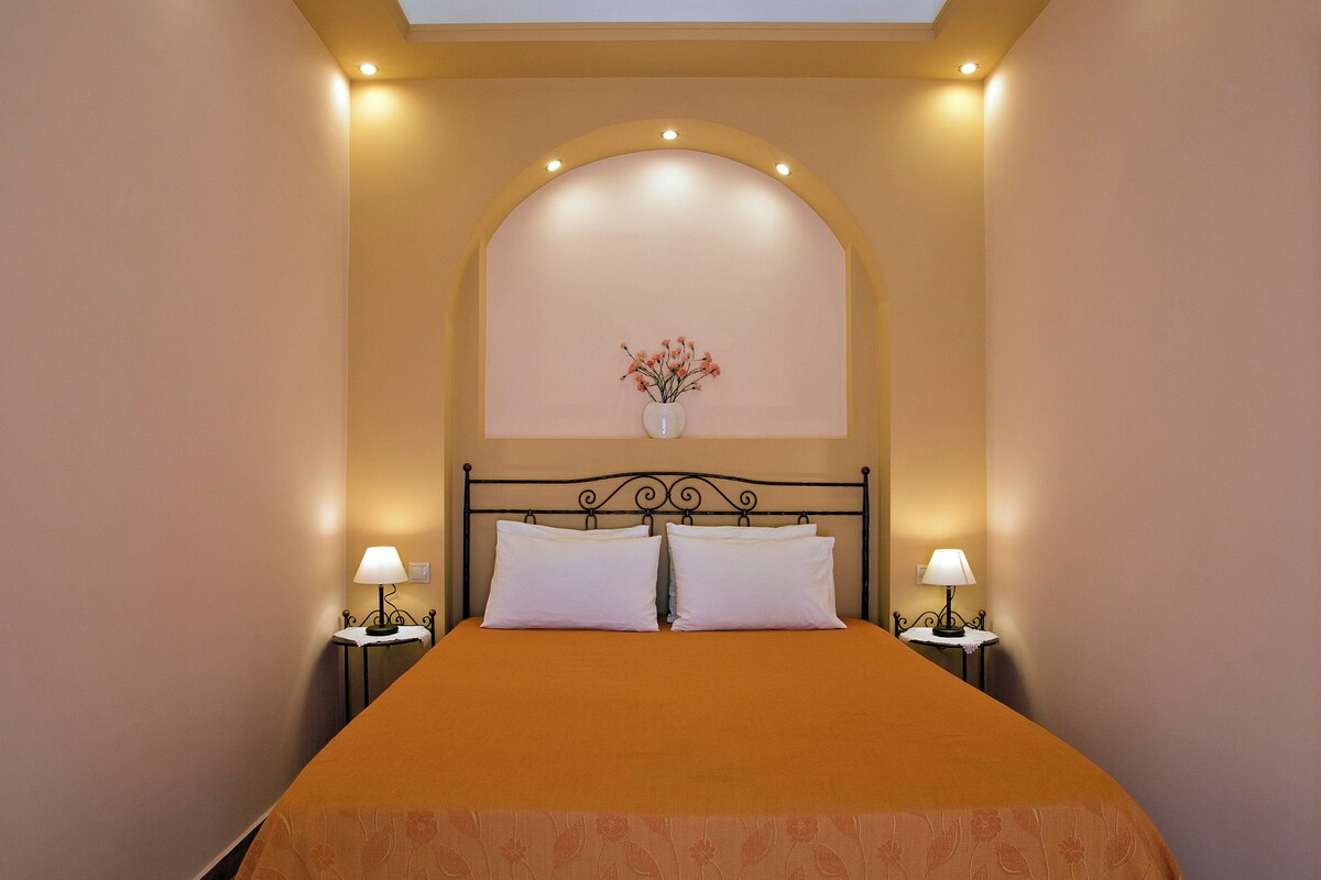 A neatly made bed with a brown bedspread, two white pillows, and a vase with flowers on the headboard. There are two bedside lamps on either side of the bed.