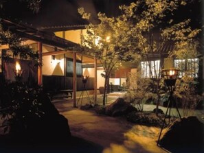 A traditional Japanese-style building with a covered outdoor seating area and a well-lit garden at night. - Yufu No Oyado Hotaru (Yufu)