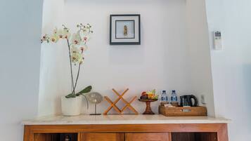Un mueble de madera con una orquídea blanca, un cuadro enmarcado, un pequeño ventilador, un frutero y una botella de agua.