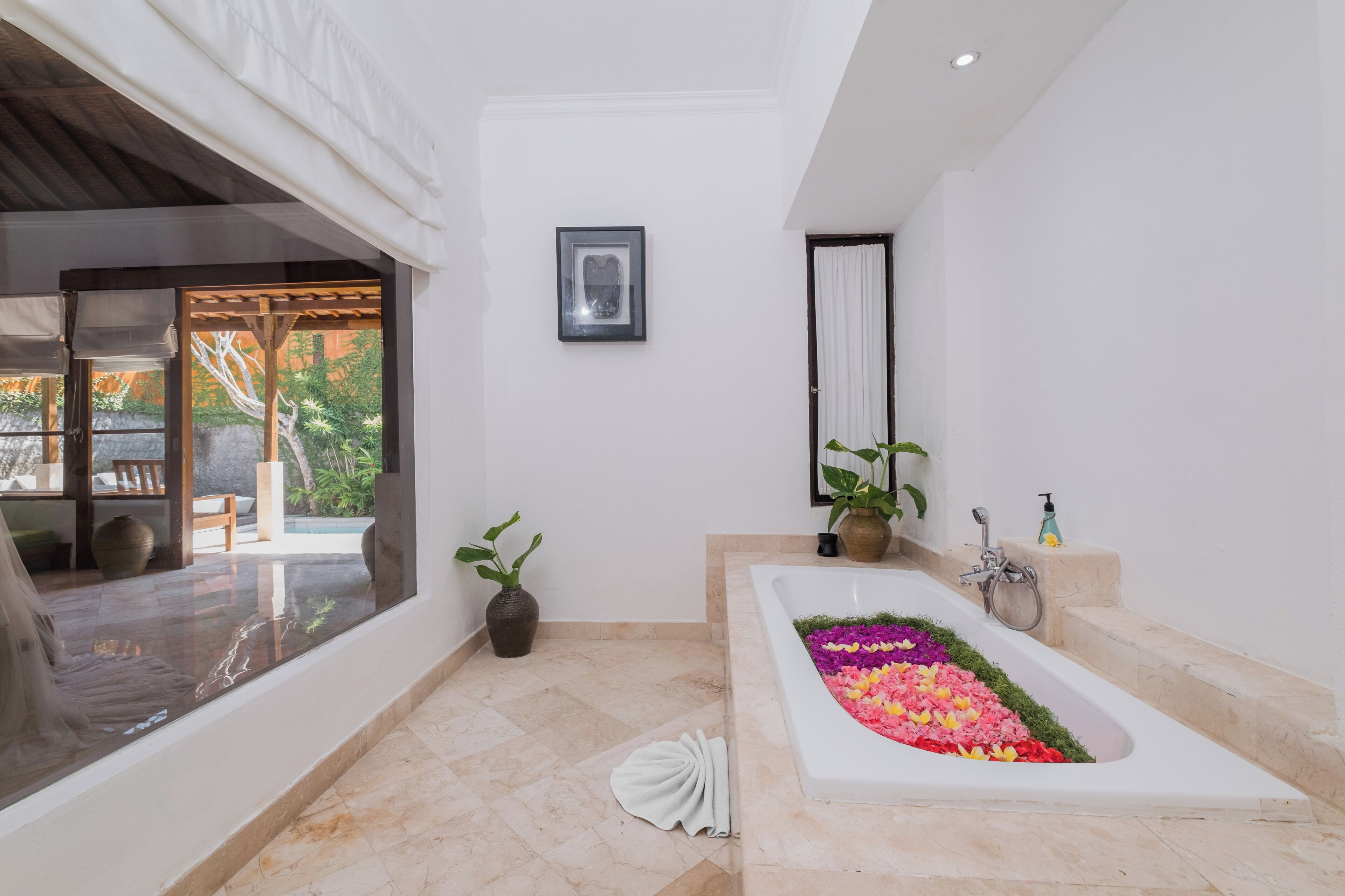 A modern bathroom with a large bathtub, a shower, and a window overlooking a garden.