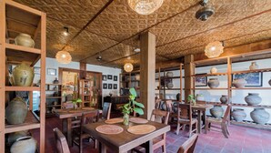 A restaurant interior with wooden furniture, shelves with pottery, and hanging lights. - Alam Bidadari Seminyak Villas (Seminyak)