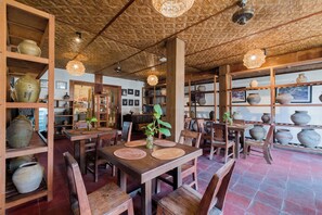 En restauranginteriör med trämöbler, hyllor med keramik och hängande lampor.