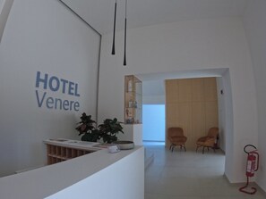 Zona de recepció d'hotel amb disseny modern, que inclou una taula de recepció, una planta i dues zones d'estar.