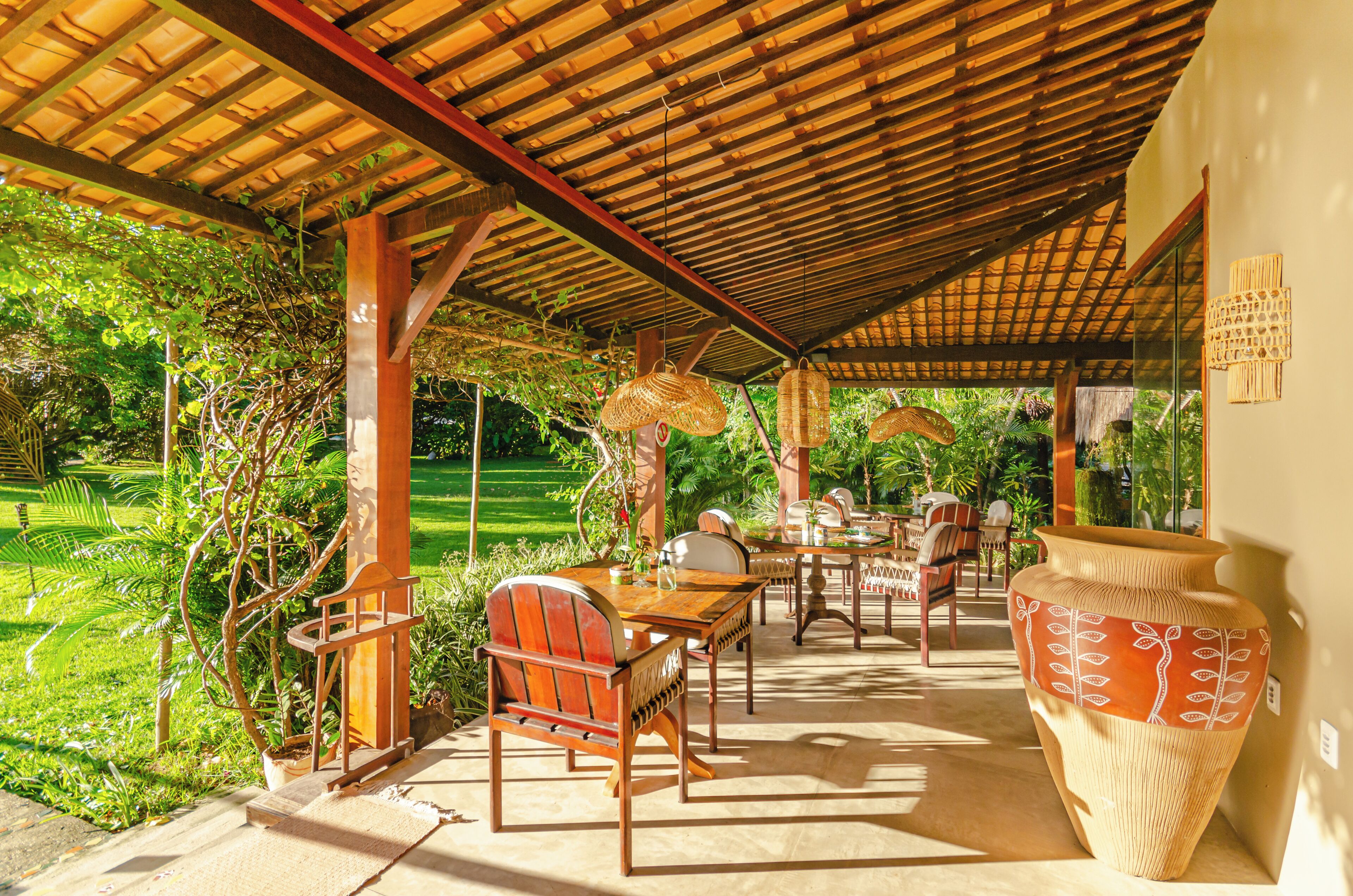 Une terrasse extérieure avec des meubles en bois, un grand vase en osier et une vue sur un jardin luxuriant.