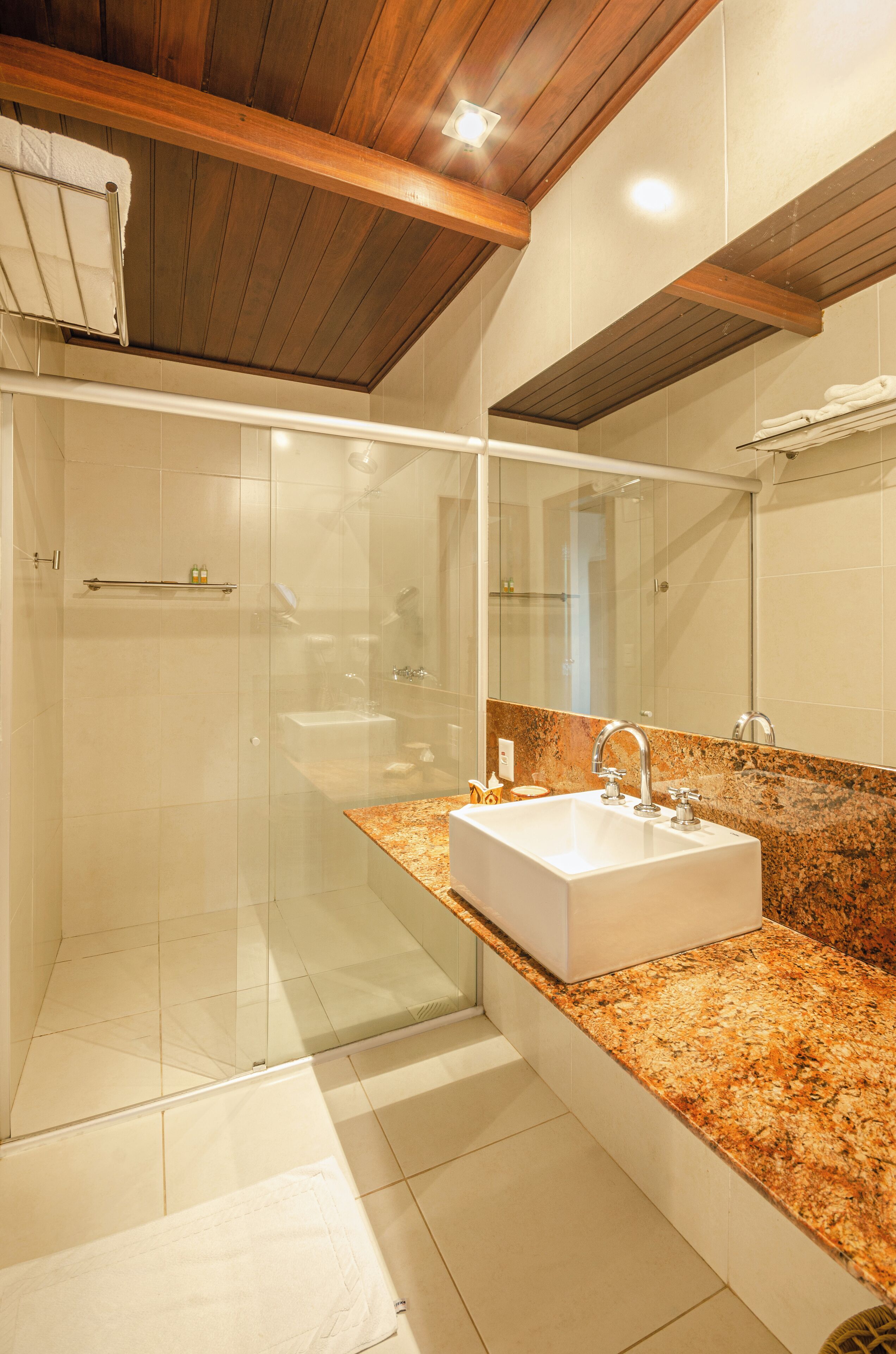 Une salle de bain moderne dotée d’un grand lavabo, d’une douche à parois de verre et de poutres en bois au plafond.