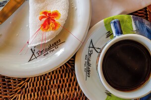 Um prato branco com decoração floral e texto, uma xícara de café e um descanso de palha.
