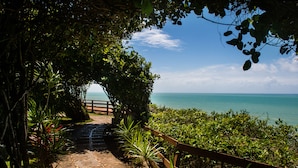 A paved pathway leading to a beach with a wooden fence and lush greenery. - Ponta do Madeiro (Tibau do Sul)