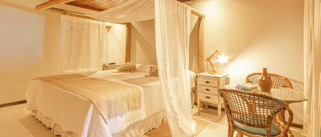 A bedroom with a four-poster bed, a bedside table with a lamp, and a wicker chair.