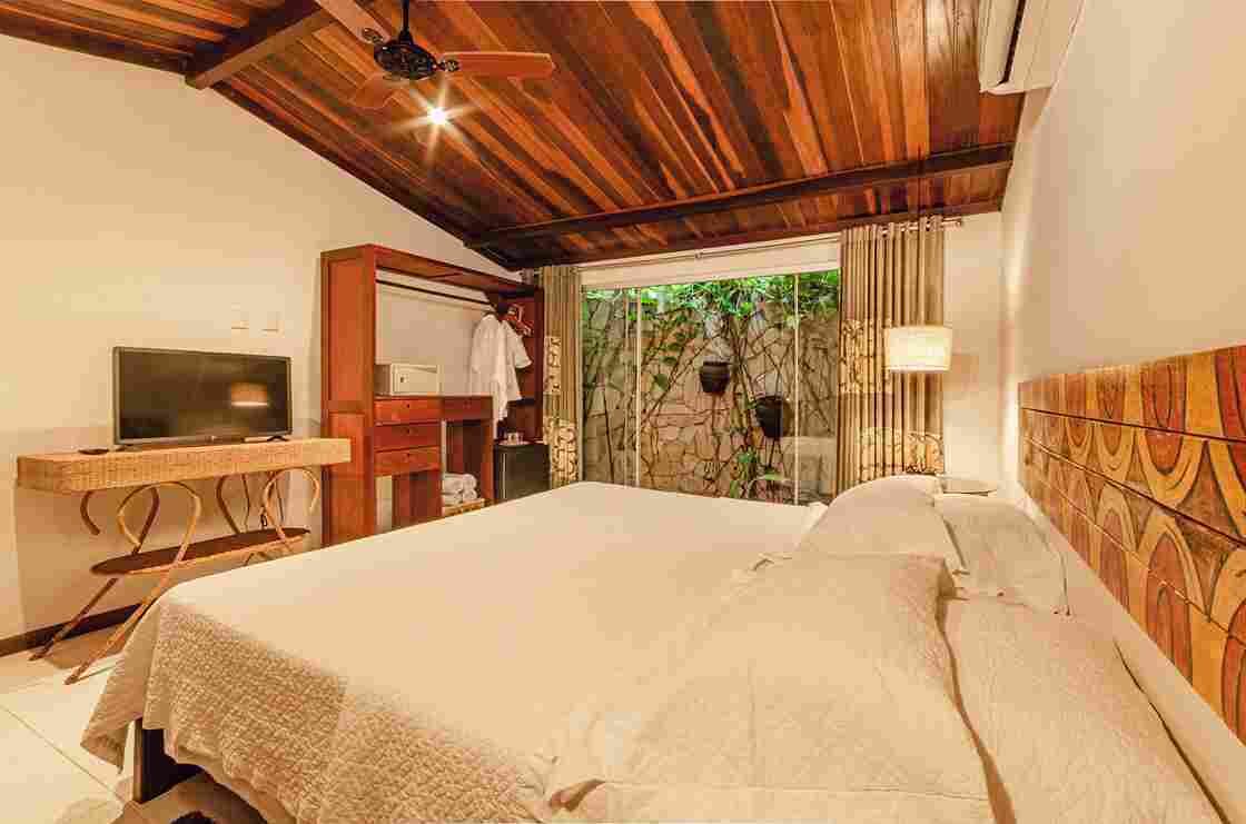 Un dormitorio con techo de madera, una cama, un televisor, un escritorio y una ventana con cortinas.