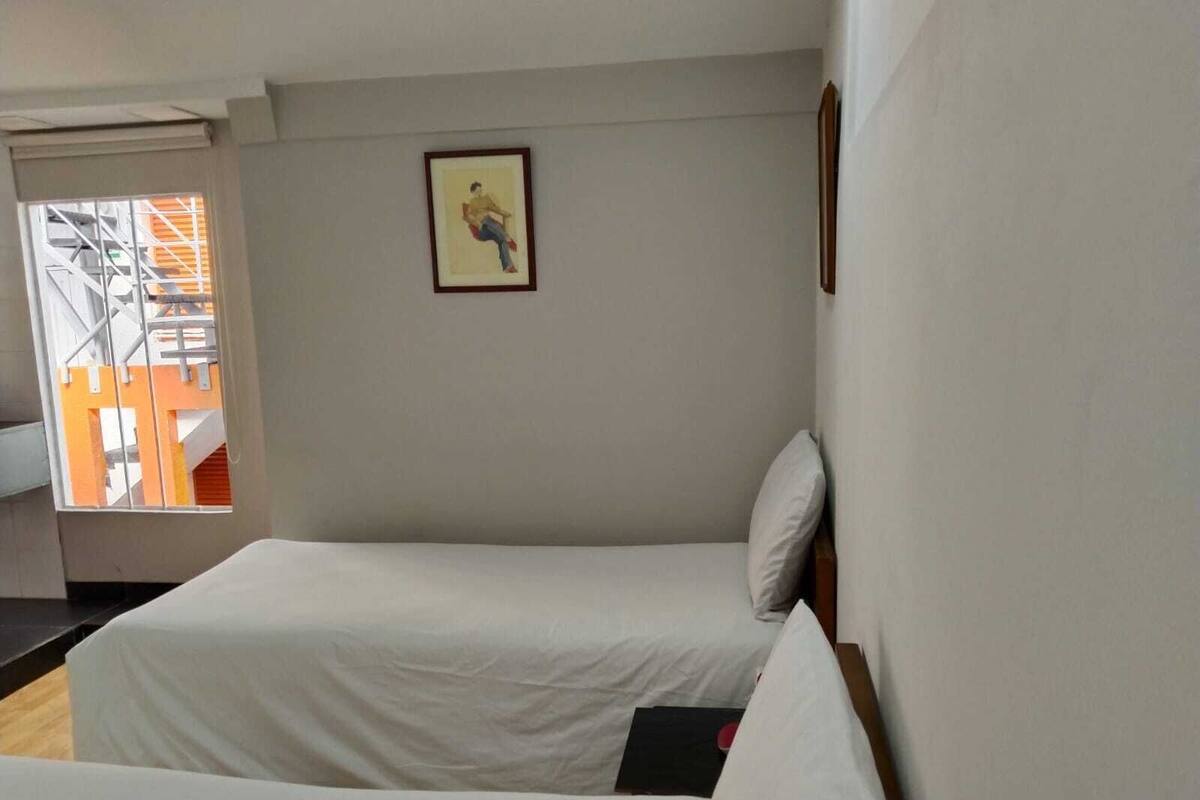 A hotel room with two beds, a window with a view of an orange building, and a framed picture on the wall.