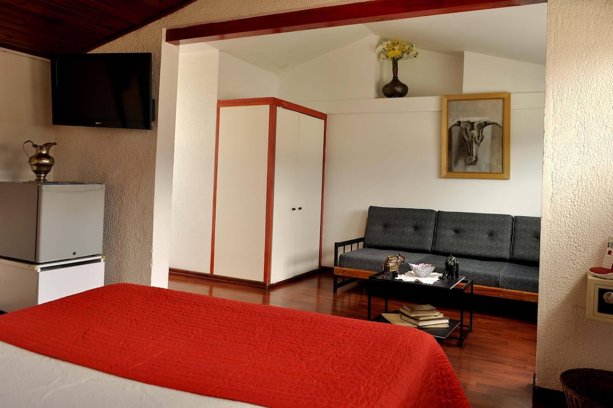 A hotel room with a bed, a sofa, a TV, a small table, and a cabinet.