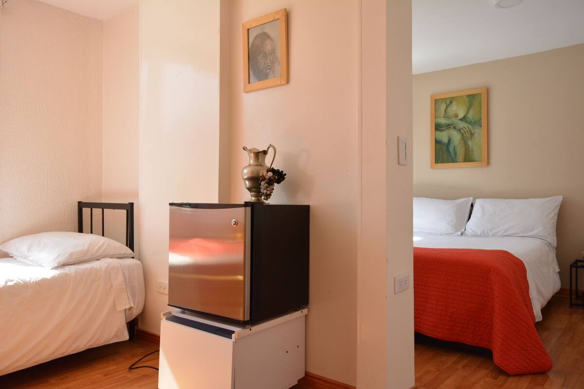 A bedroom with a bed, a small refrigerator, and a painting on the wall.