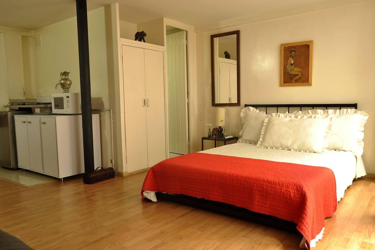 A bedroom with a bed, a wardrobe, a nightstand, and a painting on the wall.