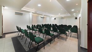 Une salle de conférence avec des rangées de chaises vertes, des murs blancs et des spots encastrés au plafond.