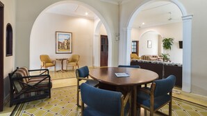 Un coin repas avec une table ronde et des chaises bleues, une porte en arc de cercle et un canapé agrémenté de coussins à motifs.