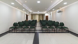 Une salle de conférence avec des rangées de chaises vertes, des murs blancs et un sol carrelé.