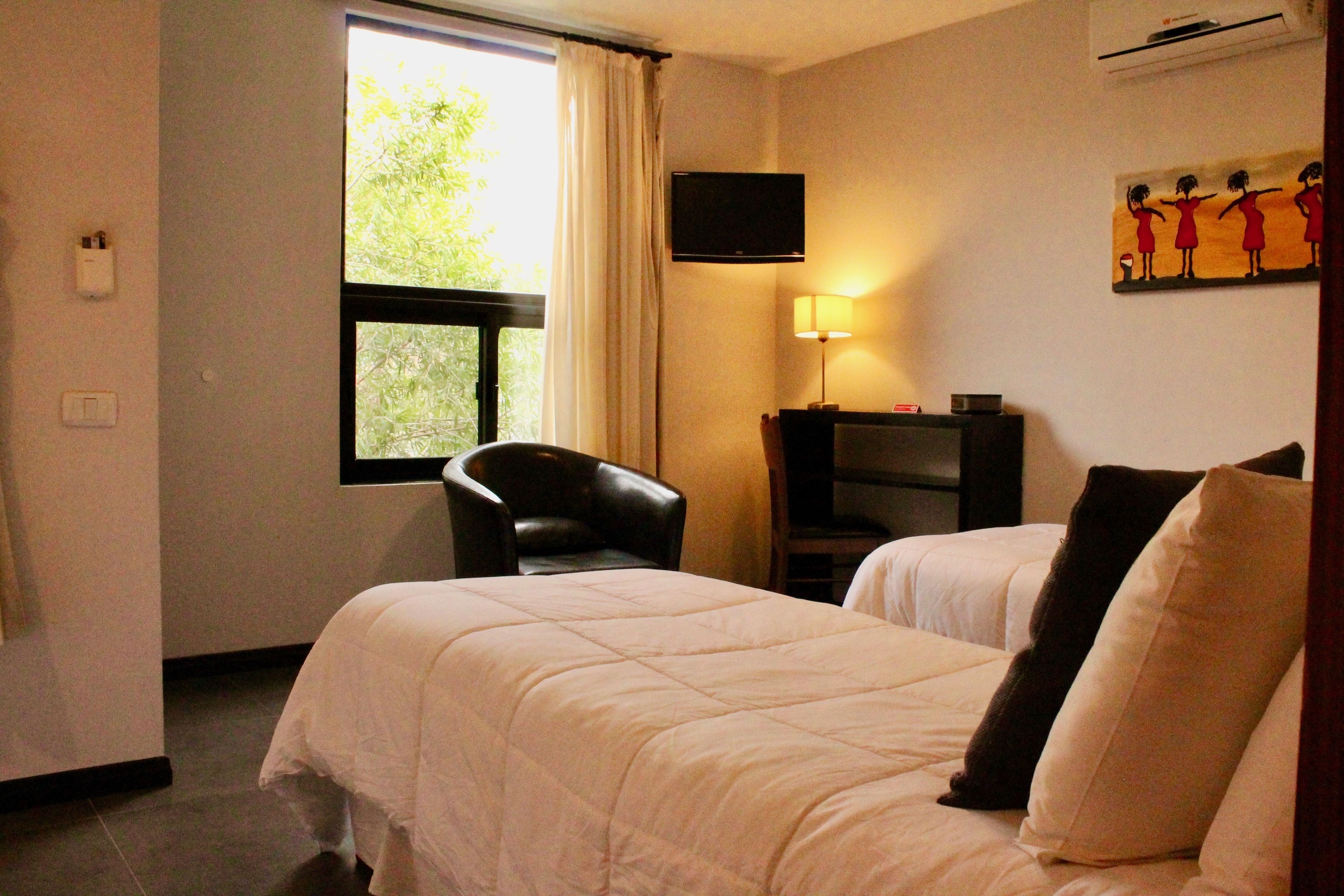 A hotel room with two beds, a desk, a chair, a TV, and a window with curtains.