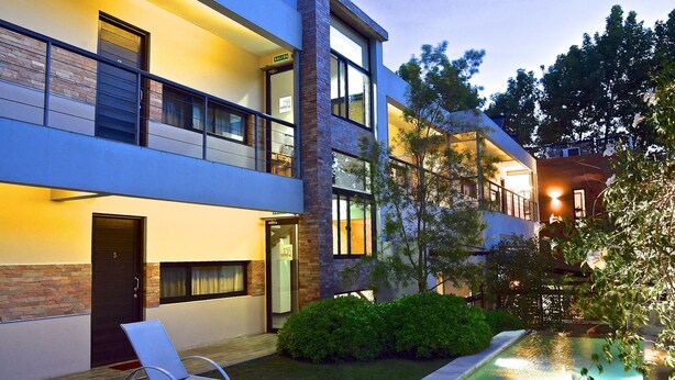 A modern building with a pool, a lounge chair, and a well-maintained garden.