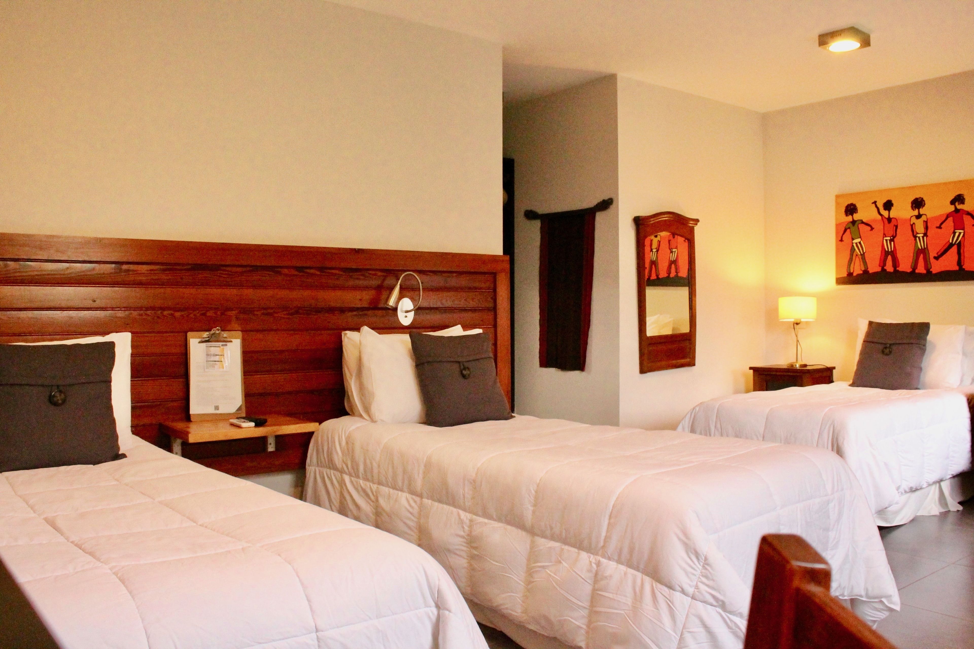 A hotel room with two single beds, wooden headboards, bedside tables with lamps, and a wall-mounted artwork.