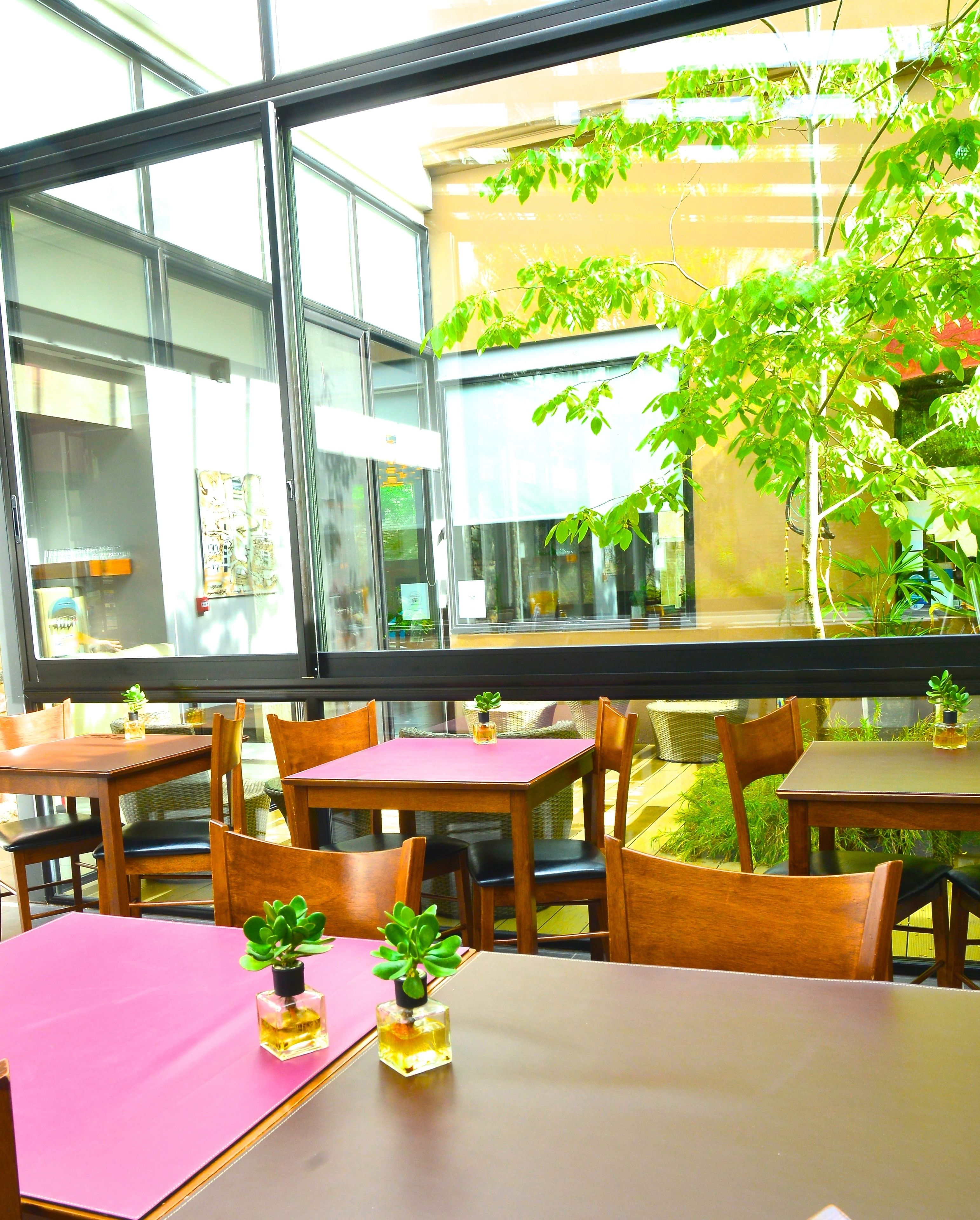 An indoor dining area with tables and chairs, large windows, and potted plants.