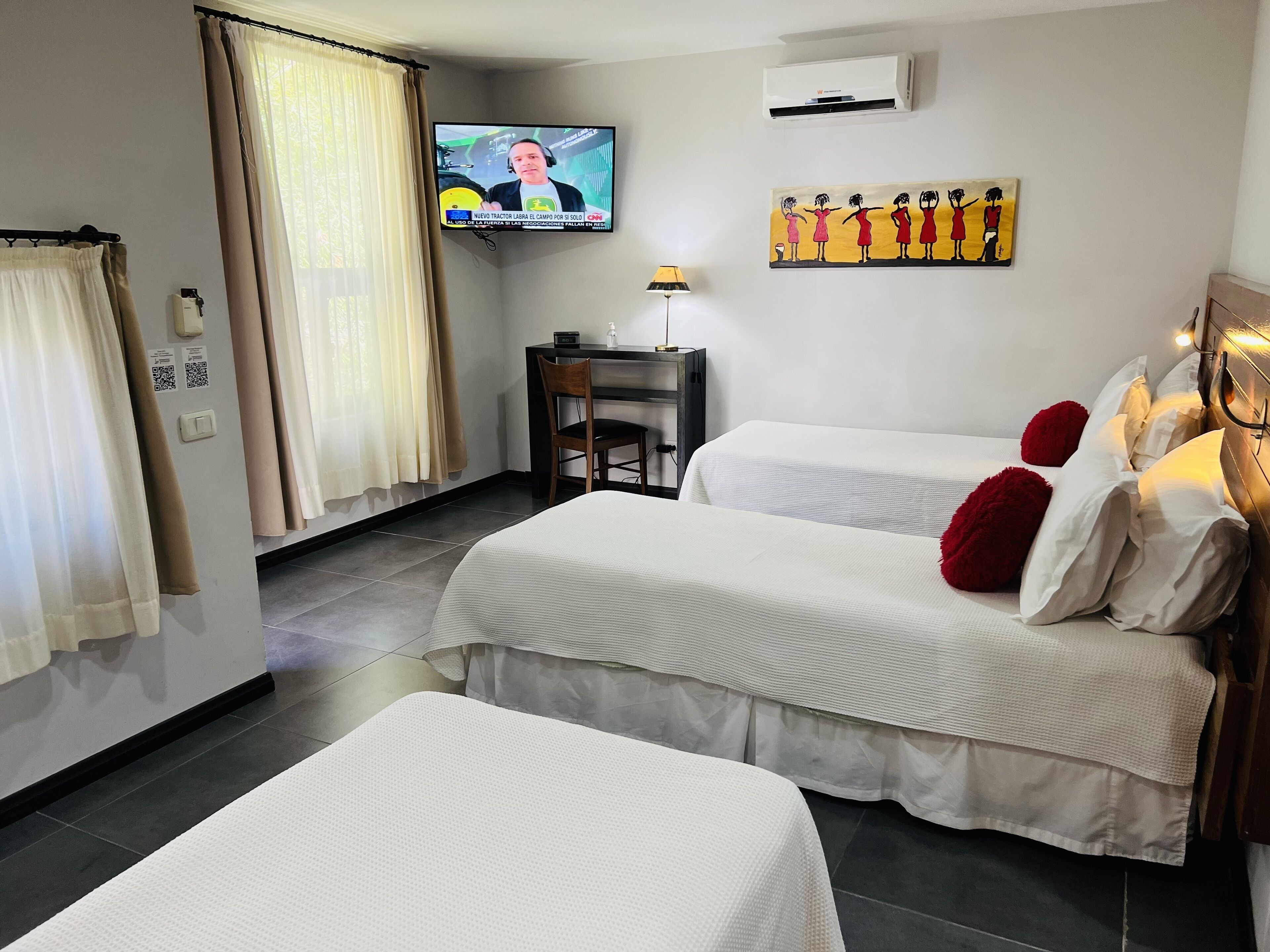 A hotel room with two beds, a television, a desk, and a painting on the wall.