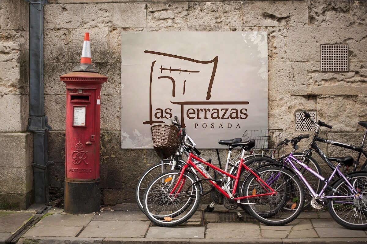 A red post box, a sign with the text "as terrazas POSADA", and two bicycles parked against a stone wall.