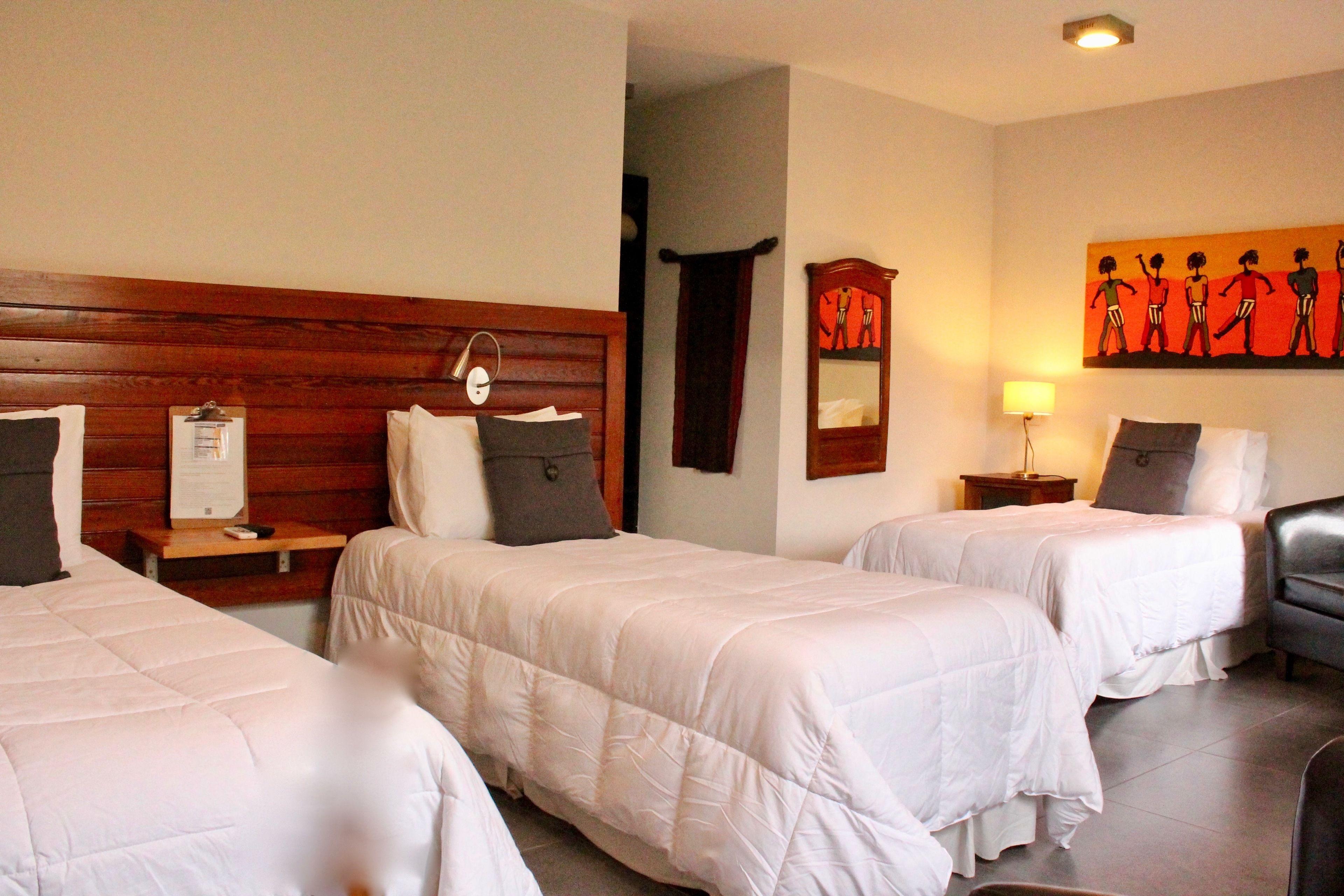 Habitación de hotel con dos camas, cabeceros de madera, mesitas de noche con lámparas, un espejo y un cuadro en la pared.