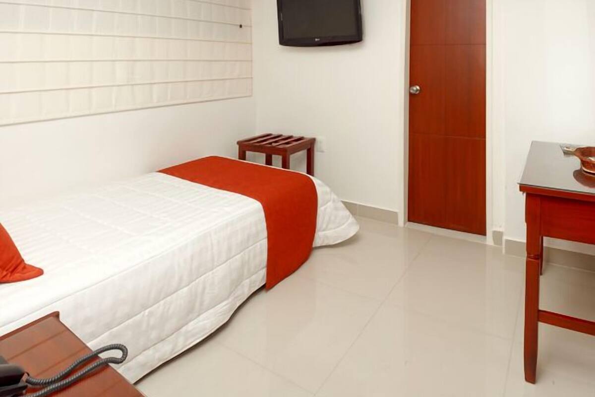 A hotel room with a bed, a desk, a chair, a television, and a door.