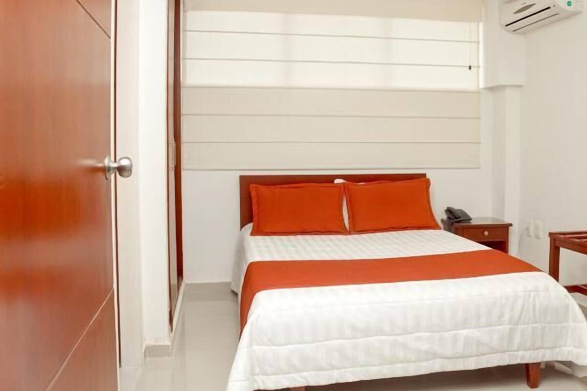 A hotel room with a bed, a nightstand, and an air conditioning unit.