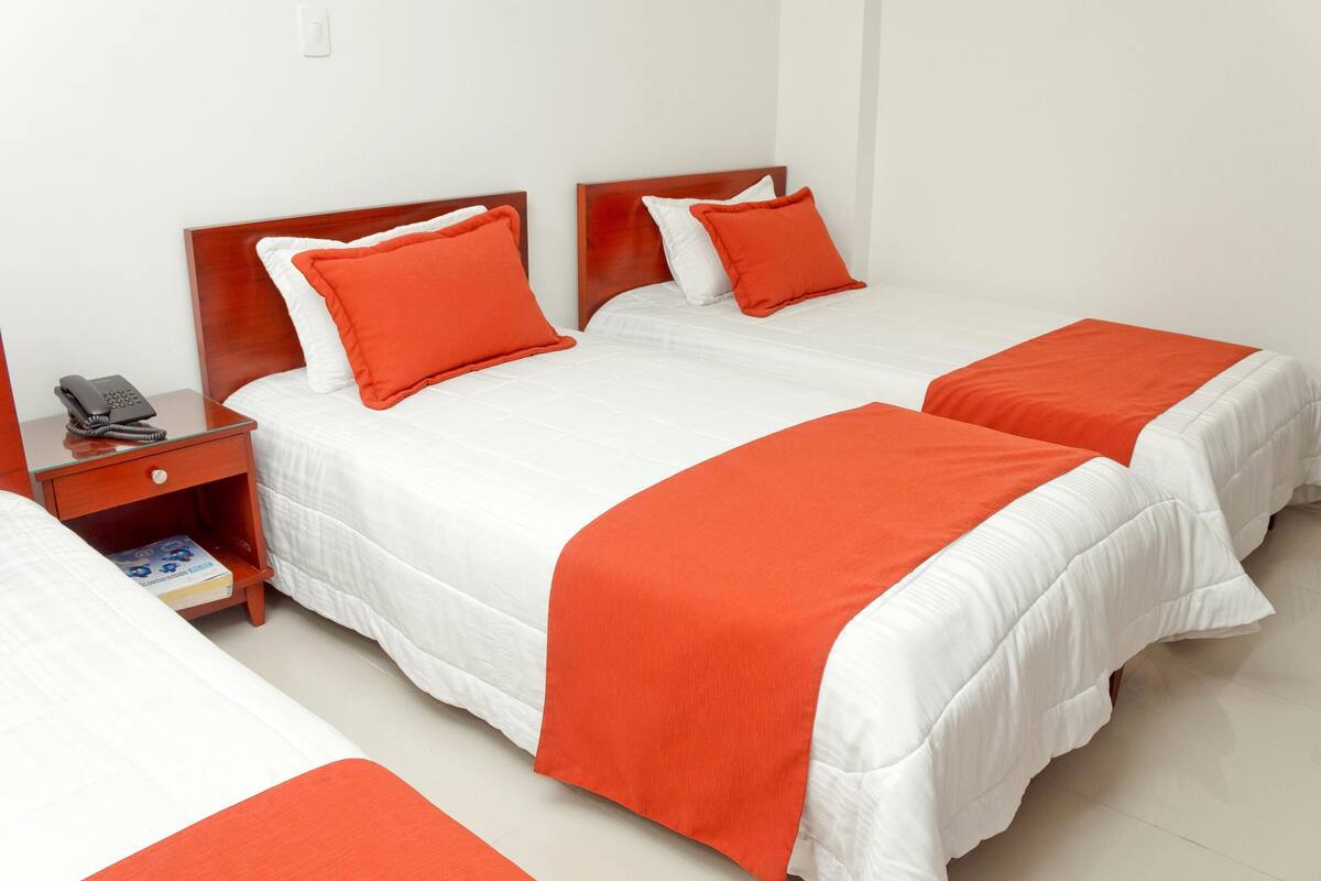 A hotel room with two beds, each with white bedding and orange accents. There is a wooden nightstand with a telephone and a book.
