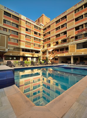 Un hotel con piscina central, varios balcones y zonas de estar al aire libre.