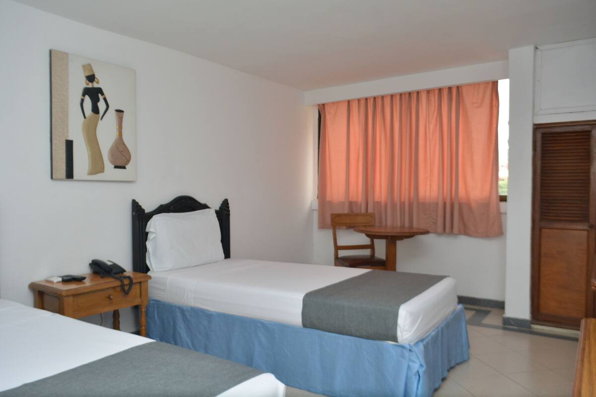 Habitación de hotel con dos camas, un escritorio con teléfono, una silla y una ventana con cortinas.