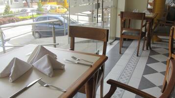 An indoor dining area with tables set for two, chairs, and a view of the street outside.