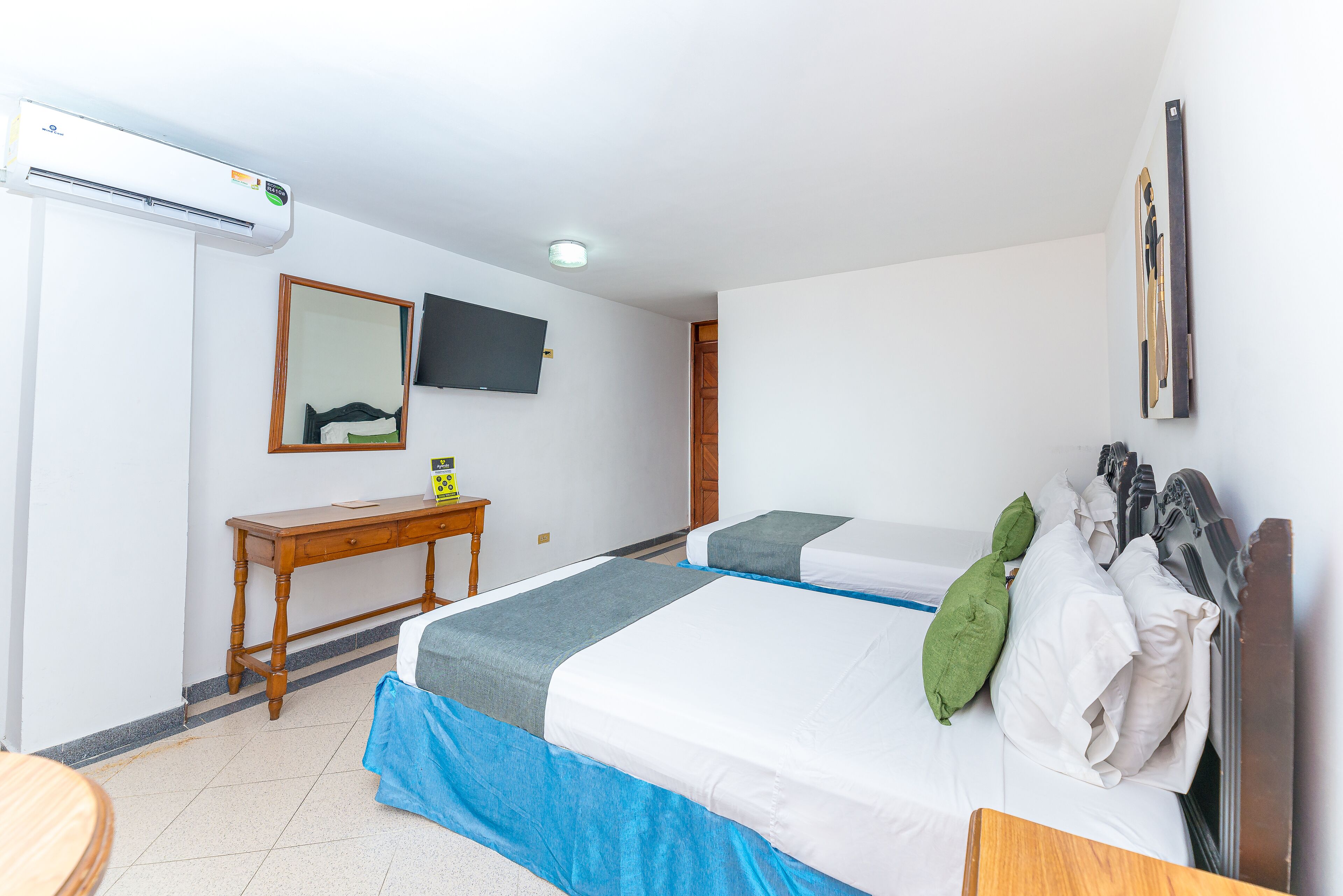 A hotel room with a bed, a desk, a mirror, a TV, and a window.