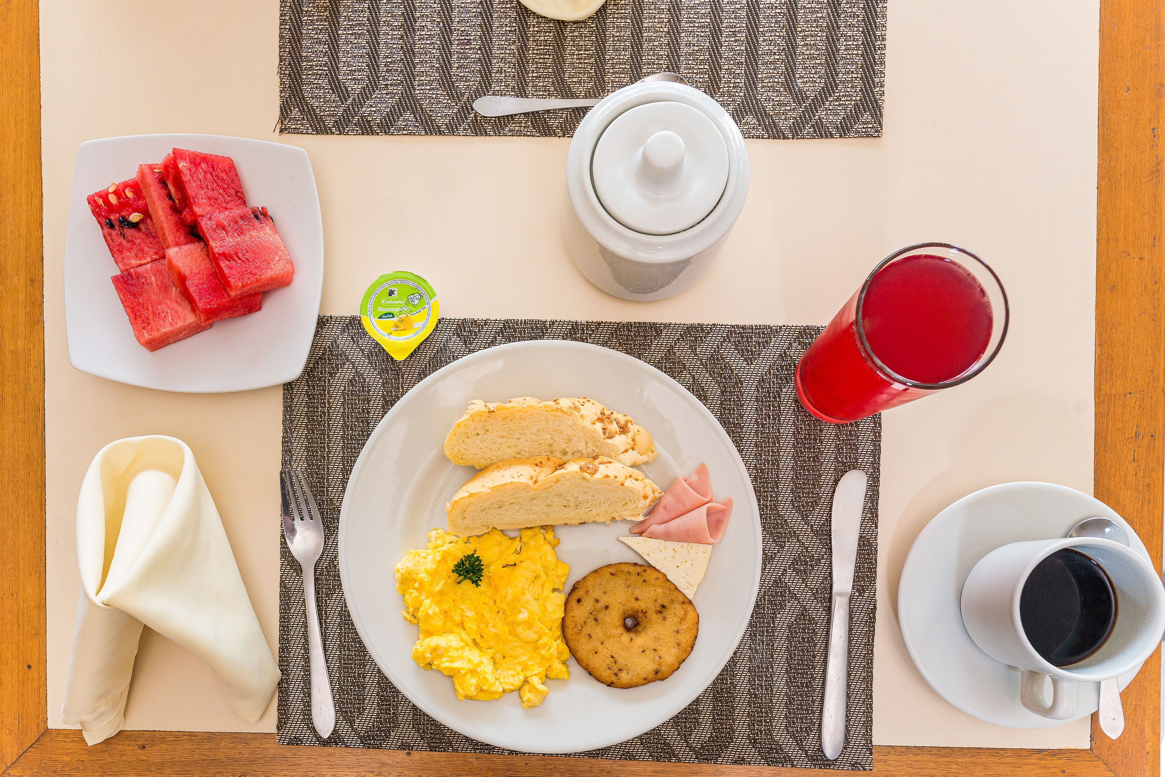 A breakfast setting with a plate of eggs, toast, ham, and a fruit slice on a table.