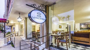 Interior de restaurant amb un cartell que diu "LA HACIENDA RESTAURANTE", una escala que porta a l'entrada i una zona de bar visible a través de portes de vidre.