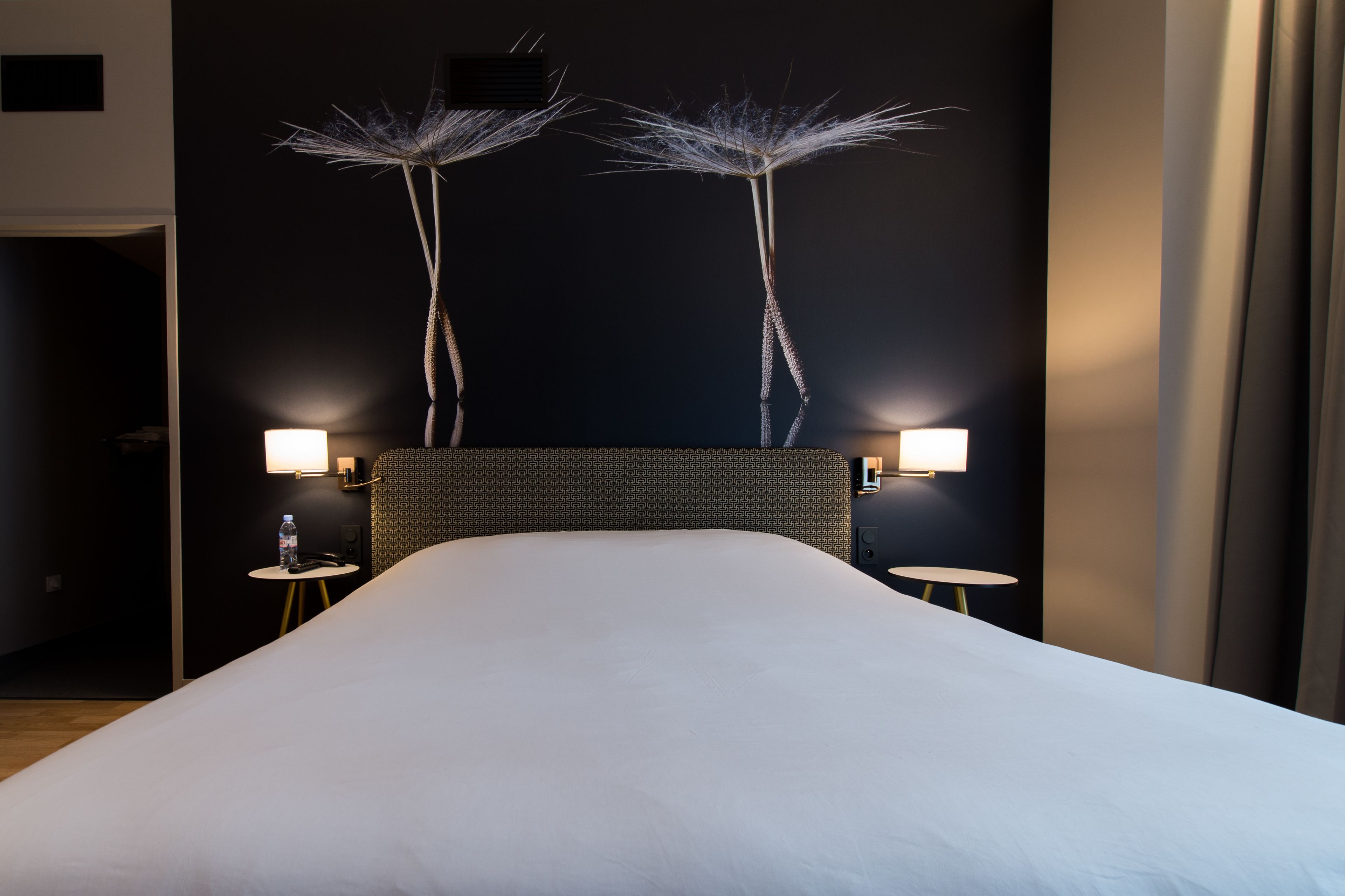 A hotel room with a large bed, two wall-mounted lamps, and a decorative wall piece.